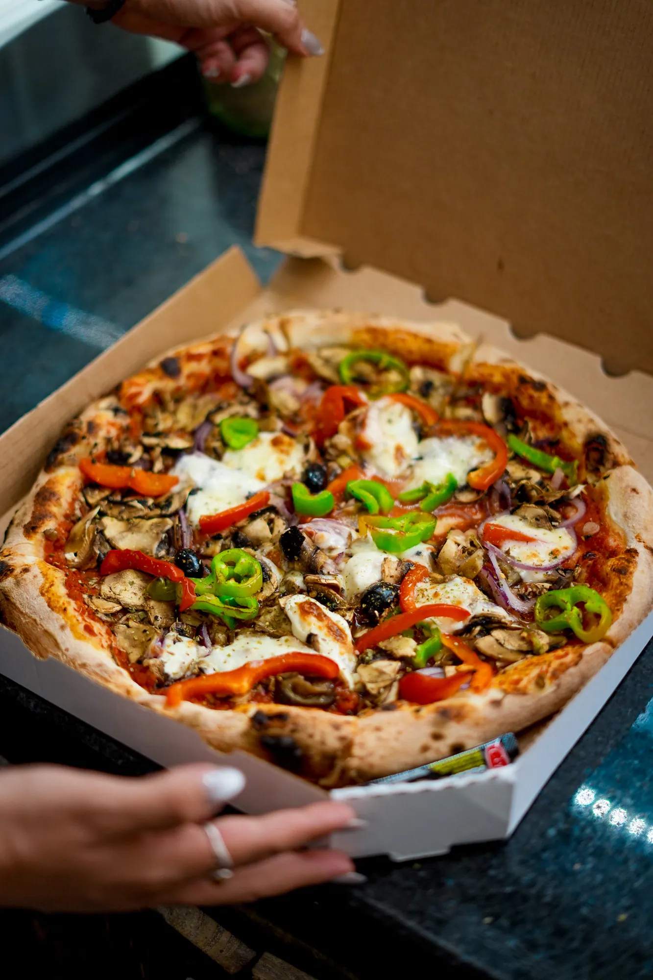 Pizza garnie dans sa boîte, sur le comptoir de la pizzeria